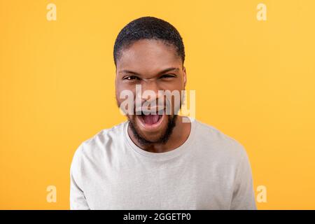 Furia. Ragazzo nero arrabbiato urla emotivamente alla fotocamera, esprimendo rabbia e aggressione su sfondo giallo studio. Concetto di emozioni negative Foto Stock