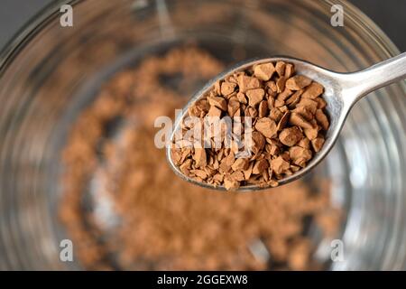 Congelare il caffè istantaneo essiccato su cucchiaino da tè con fondo tazza di caffè in vetro. Foto Stock