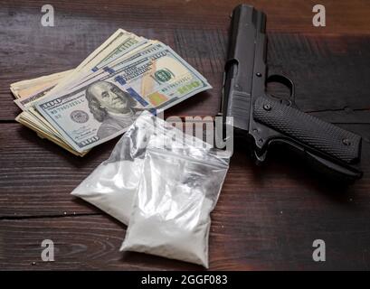 Droga narcotici concetto di business illegale. Pacchetti di plastica di cocaina, pistole e banconote in dollari USA su un tavolo. Polvere bianca dipendenza e crimine Foto Stock