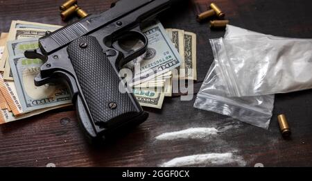 Droga narcotici concetto di business illegale. Pacchetti di plastica di cocaina, pistole e banconote in dollari USA su un tavolo. Polvere bianca dipendenza e crimine, copia Foto Stock