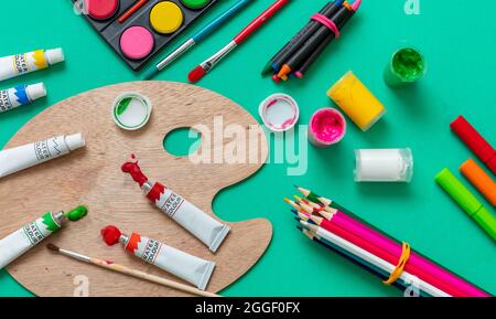 Istruzione, ritorno a scuola, concetto di creatività dei bambini. Forniture scolastiche, tavolozza di pittura e colori su sfondo verde. Foto Stock