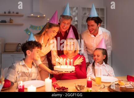 Famiglia allegra di multi generazione che ha festa di compleanno in serata, presentando torta donna anziana con candele, godendo la vacanza, avendo grande tempo di Toge Foto Stock