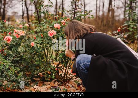 una donna di viaggio in moda autunno vestiti sniffing i fiori di rosa nel parco autunnale. concetto di viaggio locale Foto Stock