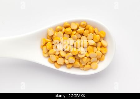 Macro primo piano di Bram Bengala biologico (Cicer arietinum) o chana dal giallo diviso su un cucchiaio per zuppa di ceramica bianca. Vista dall'alto Foto Stock