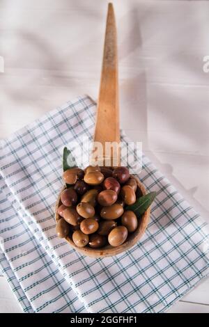 Presentazione di un piccolo gruppo di olive nere su mestolo di legno Foto Stock