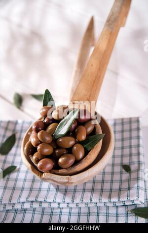 Presentazione di un piccolo gruppo di olive nere su mestolo di legno Foto Stock