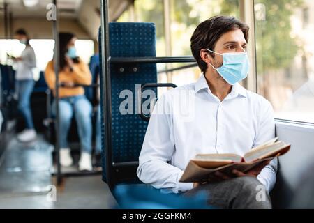 Ritratto di uomo pensivo in maschera usa e getta tenendo libro, andare a casa o a lavorare in autobus, guardando da parte attraverso la finestra e il pensiero. Tipo di rea pensivo Foto Stock