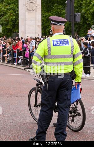 Londra, Inghilterra - Agosto 2021: Vista posteriore di un ufficiale di polizia Metropolitan che indossa una giacca riflettente. Sullo sfondo ci sono folle di persone. Foto Stock