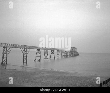 Anni '50, storica, la passerella in legno e la vecchia stazione di scialuppa di salvataggio a Selsey, West Sussex, Inghilterra, Regno Unito. Un servizio di scialuppa di salvataggio è stato istituito a Selsey nel 1861. Nel 1927 per ospitare il nuovo motonave della stazione, la casa barca è stata costruita e questa struttura è visibile nella foto. Questa stazione di scivoli fu nuovamente ricostruita alla fine degli anni '50, ma fu abbassata nel 2017. Foto Stock