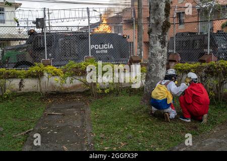 26 agosto 2021, PopayÃn, Colombia: I manifestanti si nascondono dietro un albero dopo aver gridato un cocktail molotov su un carro armato di polizia durante una protesta a Popayan.i manifestanti si confrontano con la polizia per protestare contro l'assassinio di Esteban Mosquera, un leader studentesco e attivista anti-polizia per la brutalità a PopayÃn. La protesta fa parte di un continuo sciopero nazionale che ha avuto inizio in Colombia il 28 aprile in reazione a riforme fiscali che sarebbero destinate ai più poveri del paese. (Credit Image: © David Lombeida/SOPA Images via ZUMA Press Wire) Foto Stock