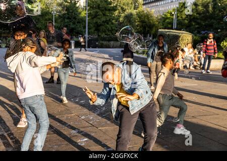 Le famiglie possono divertirsi lungo la Southbank di Londra mentre un artista soffia grandi bolle sul marciapiede, Inghilterra, Regno Unito. Foto Stock