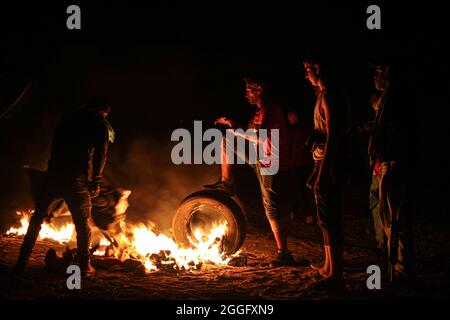 Territori palestinesi, striscia di Gaza. 31 agosto 2021. I dimostranti palestinesi bruciano pneumatici di gomma durante gli scontri con l'esercito israeliano soprannominato "confusione notturna” lungo la striscia di confine che separa la striscia di Gaza e Israele a est di Khan Yunis nella striscia meridionale di Gaza, protestando contro il blocco in corso sulla striscia di Gaza. Gaza. Foto Stock