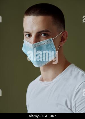 un uomo in una t-shirt bianca che indossa una maschera medica ritratto primo piano scuro sfondo Foto Stock