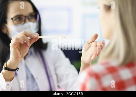 Medico femmina che esamina la gola del paziente con spatola di legno closeup Foto Stock