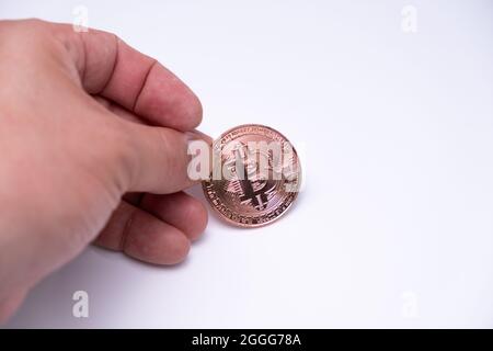 Dito mano maschio che tiene sulla moneta da tavolo bitcoin criptovaluta. Da vicino a moneta oro rosa in piedi su sfondo bianco. BTC valuta più popolare Foto Stock