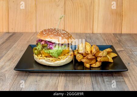 Delizioso hamburger di manzo messicano con guacamole e formaggio cheddar fuso, jalapenos e cipolla rossa con un lato di patate di lusso Foto Stock