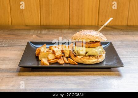 Hamburger di manzo con formaggio fuso con foie gras e pancetta fritta, patatine fritte e pane con semi di sesamo Foto Stock