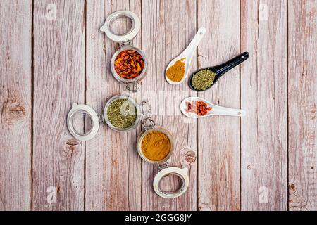 Aprire vasetti di spezie ermetici e cucchiai di porcellana riempiti di origano, curry e cayenne su un tavolo leggero Foto Stock