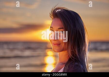Ritratto di donna sorridente 31 anni all'aperto durante il tramonto sulla spiaggia. Foto Stock