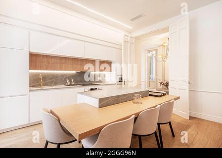 Tavolo in rovere e marmo grigio su un'isola di cucina in stile americano bianco con tonalità bianche e legno chiaro in appartamento affitto per le vacanze Foto Stock