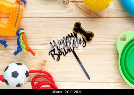 Diversi accessori multicolore per la cura degli animali domestici: Anello, ossa, palle, spuntini su sfondo naturale in legno. Accessori in gomma e tessuto per cani.Vista dall'alto Foto Stock