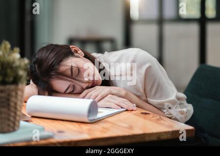 Donna d'affari stanca e sovraccarica. Giovane ragazza esausta che dorme sul tavolo durante il suo lavoro imprenditore, lavoratore freelance o studente in stress Foto Stock