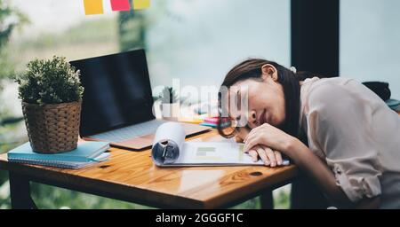 Donna d'affari stanca e sovraccarica. Giovane ragazza esausta che dorme sul tavolo durante il suo lavoro imprenditore, lavoratore freelance in concetto di stress Foto Stock