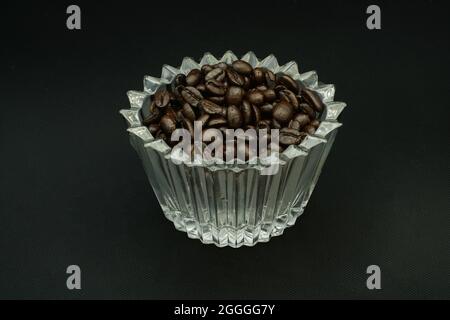 Chicchi di caffè in una tazza di cristallo su sfondo nero Foto Stock