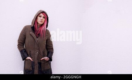 giovane donna con pelo rosa parka con cappuccio e tatuaggi contro la parete con spazio copia Foto Stock