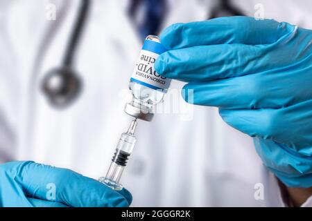 Un medico preleva il liquido da una fiala di vetro etichettata COVID-19 Vaccine. Foto Stock