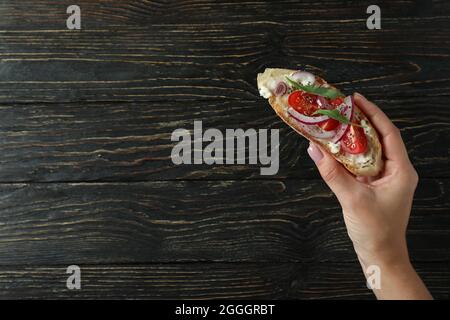 La mano femmina tiene la bruschetta su sfondo rustico in legno Foto Stock