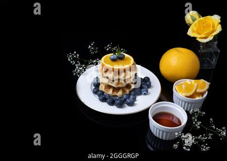 Tavolo per la colazione composto da waffle con miele, mirtilli e arancia. Foto Stock