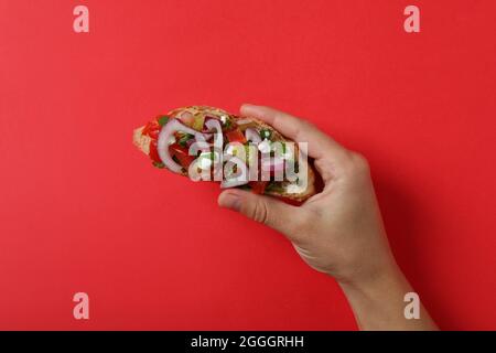 La mano femmina tiene la bruschetta su sfondo rosso Foto Stock