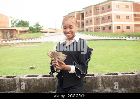 Grande vittoria! Scioccata e felice ragazza africana che tiene un sacco di soldi Foto Stock