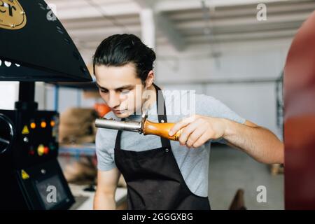 Primo piano del giovane uomo che controlla la qualità dei chicchi di caffè arabica appena tostati Foto Stock