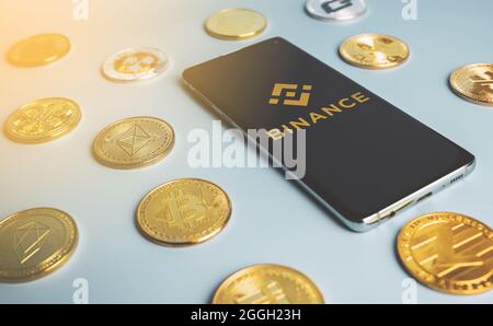 Logo dell'app Binance su uno smartphone tra le monete criptate su sfondo blu. Popolare scambio di criptovaluta. Swansea, Regno Unito - 29 agosto 2021. Foto Stock