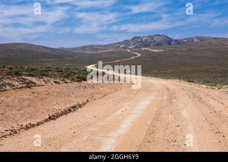 Una lunga strada sterrata che porta in lontananza alle montagne Foto Stock