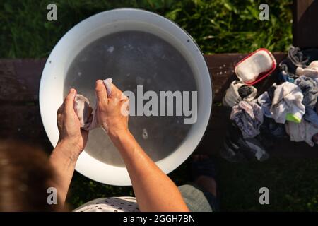 La donna lava i vestiti con le mani in un vecchio lavandino con un sapone all'aperto Foto Stock