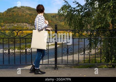 Donna che porta la borsa vuota che guarda il mockup fiume. Borsa tote eco-compatibile con tele da tenuta a mano femmina Foto Stock