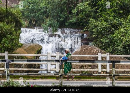 Old Woman Walking di fronte alla cascata di Ramboda, Nuwara Eliya, Sri Lanka Foto Stock