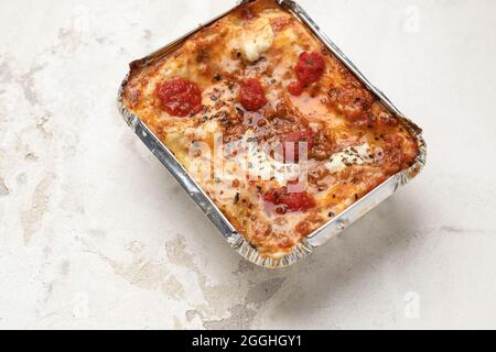 Togliere la lasagna cremosa con mozzarella fresca e pomodori su fondo di argilla bianca Foto Stock