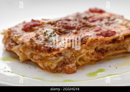 Togliere la lasagna cremosa con mozzarella fresca e pomodori sul piatto bianco macro close up Foto Stock