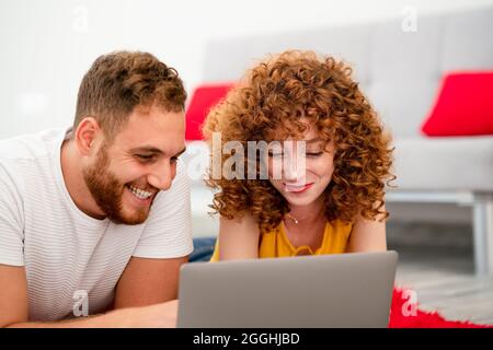 Una giovane coppia amanti o amici che si stendano su un tappeto rosso pluffy e utilizzando un computer portatile. Foto di alta qualità Foto Stock