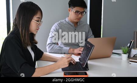 Gli uomini d'affari analizzano le classifiche delle scorte su un tablet PC mentre si trovano in un ambiente di lavoro moderno. Foto Stock