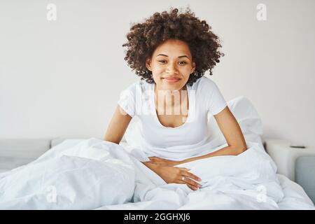 Felice attraente afroamericana donna seduta a letto Foto Stock