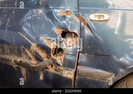Danni arrugginiti al parafango sinistro e alla porta anteriore di una vecchia auto. Foto Stock
