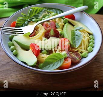 Insalata di pasta con piselli verdi, avocado, pomodori ciliegini e basilico su sfondo rustico in legno. Vista dall'alto Foto Stock