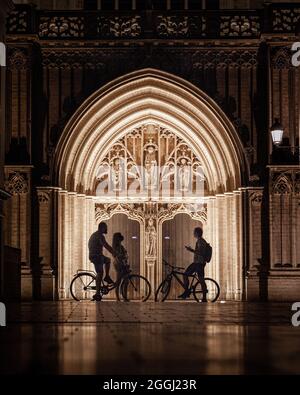 ANVERSA, BELGIO - 15 lug 2021: Un colpo verticale notturno di tre amici con biciclette che parlano contro l'arco alleggerito con sculture Foto Stock