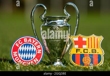 27 agosto 2021 Baviera, Monaco di Baviera. Gli emblemi dei club calcistici FC Barcelona e FC Bayern Monaco e della UEFA Champions League Cup sul prato verde o Foto Stock