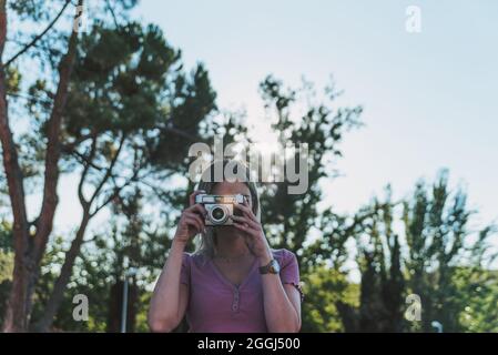 Ragazza bionda che scattano una foto con una fotocamera retrò. Sfondo dell'albero. Foto Stock